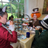 a family is dressed up inspired by the Wonderland characters of the Mad Hatter, Alice, White Rabbit sitting at a table enjoying cups of tea