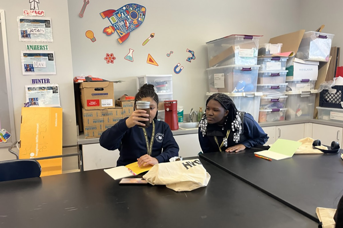 Students in a classroom observe a jar of soil.